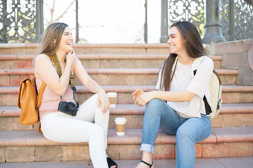 Cheerful young women sitting on steps in park during weekend trip