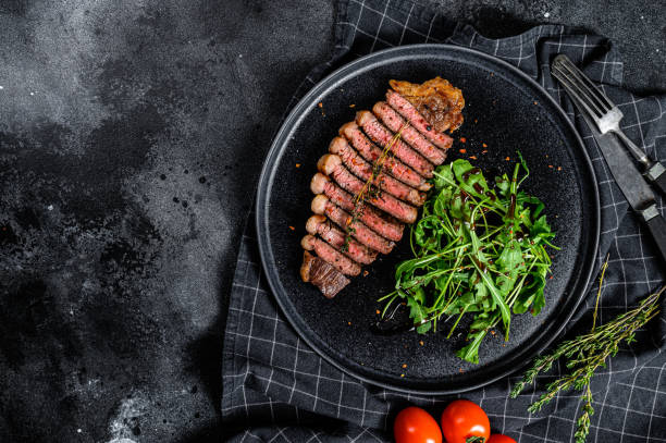 istock Sliced sirloin steak, marbled beef meat with arugula. Black background. Top view. Copy space 1254287254