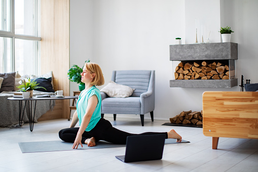 Mujer joven practicando yoga en casa con portátil durante la cuarentena photo