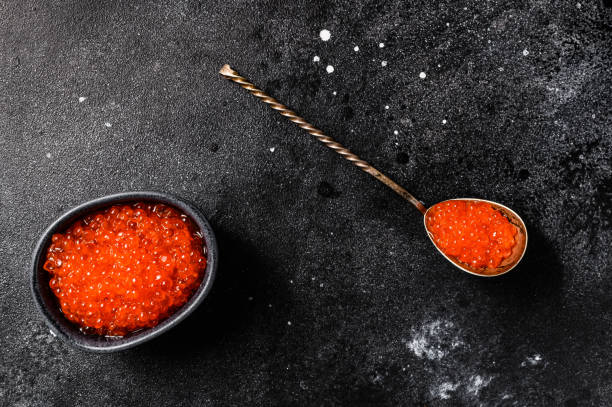 istock Salmon red caviar in an exquisite spoon. Black background. Top view 1254290274
