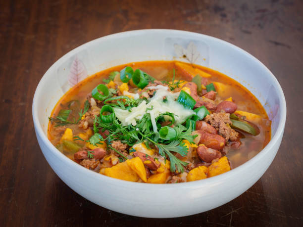 Chili with sweet potato, scallion and cheese served in a round bowl on rustic table