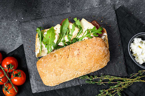 Ciabatta sandwich with fresh goat cheese, pear marmalade and arugula. Black background. Top view.
