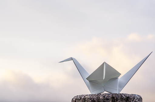 White origami crane. The traditional Japanese art of paper folding with sky and clouds in the background.
