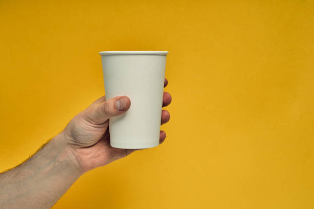 istock Paper cup in hand on a colored background. Eco-friendly materials in a coffee shop, biodegradable disposable tableware. Close up 1254302367