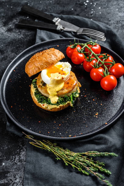 istock Delicious fishburger with fish fillet, egg and spinach on a brioche bun. Black background. Top view 1254303877