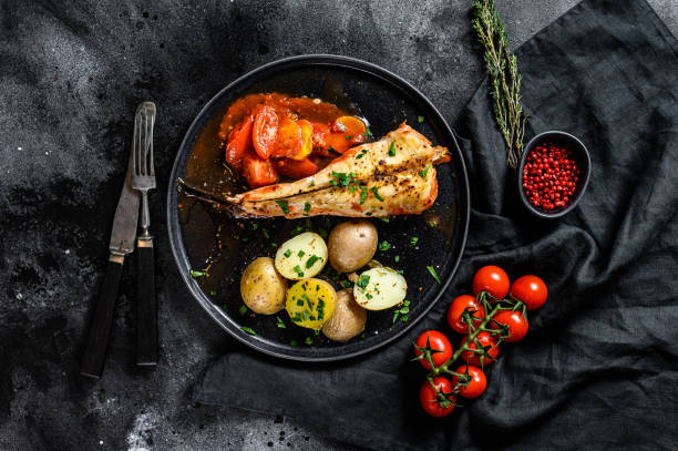 istock Baked in tomatoes monkfish with potatoes and vegetables. Black background. Top view 1254304534