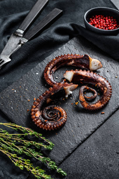 istock Fried octopus tentacles with thyme and pink pepper. Fresh seafood. Black background. Top view 1254305368