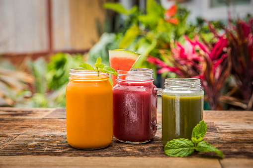 Three colorful fruit smoothie drinks in retro glass jar bottles on a old wooden background