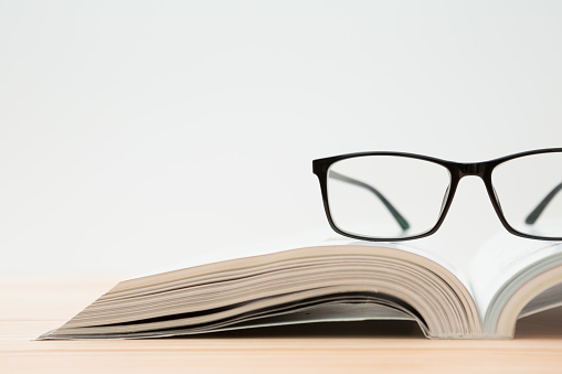 Glasses and open book on wooden table, white background and copy space