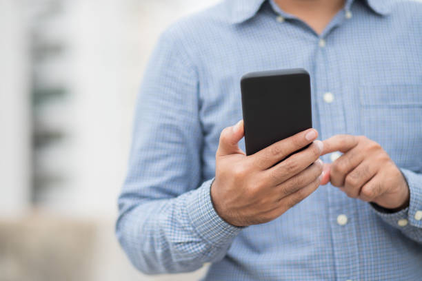 istock Close up male hands holding using black smartphone on city background. 1254326136