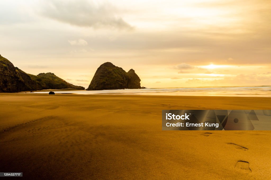 Footprints at Piha Beach Sandal / Jandal steps are reflected in the black sand at sunset. Footprint Stock Photo