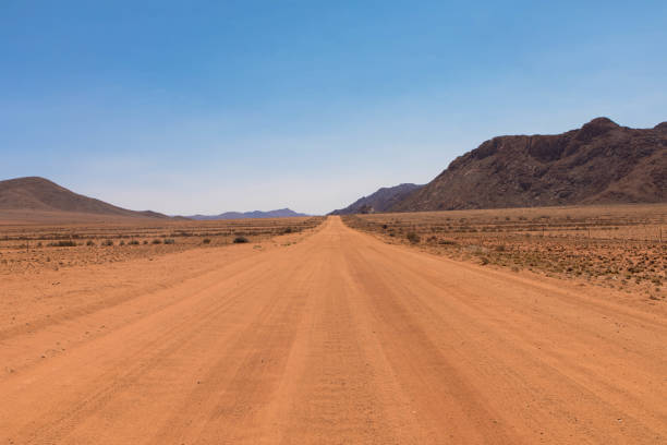 strada dritta in ghiaia che attraversa il colorato deserto del namib, nel maestoso parco nazionale namib naukluft - dirt road road desert road gravel foto e immagini stock