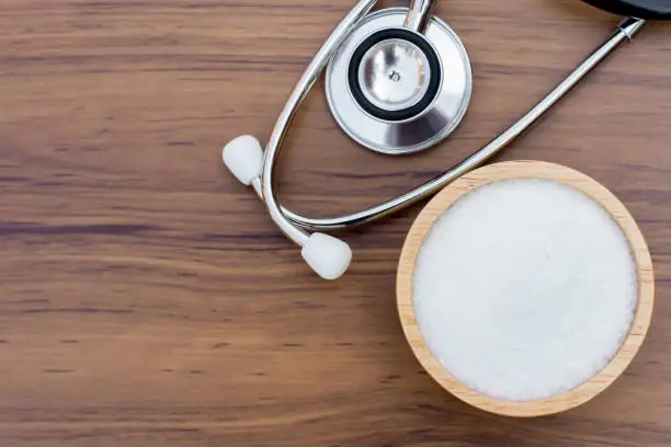 Monosodium glutamate (MSG ), ingredients in wooden bowl and words " MSG " with medical stethoscope isolated on the wood table background. Unhealthy food concept. Top view. Flat lay