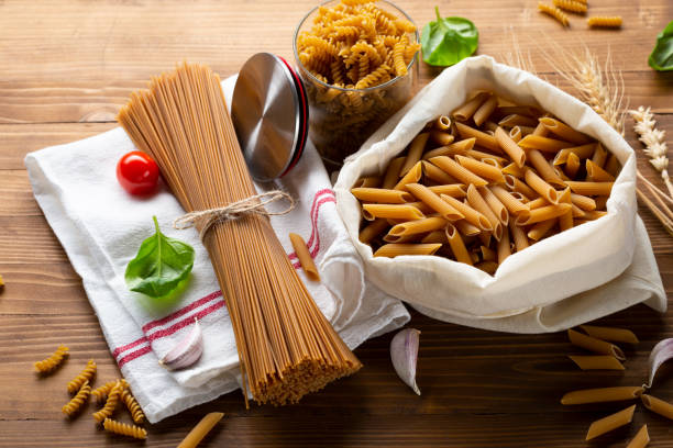 spaghetti integrali e penne su tavola di legno - pasta whole wheat spaghetti raw foto e immagini stock