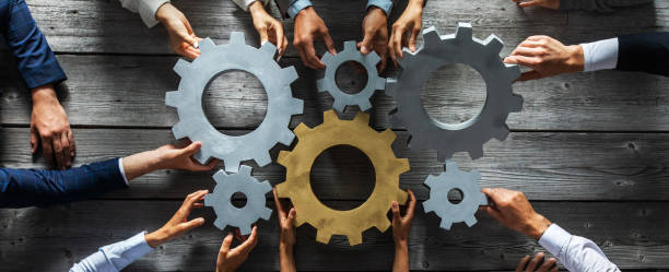 Business people joining gears Group of business people joining together silver and golden colored gears on table at workplace top view engine photos stock pictures, royalty-free photos & images