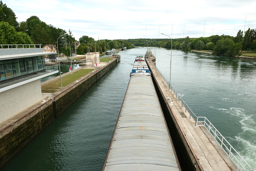 04 July 2020. Dam on the river Seine south of Paris. Barge in a lock that fills with water to pass the drop.