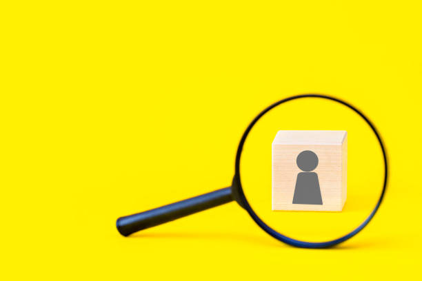 istock Search for talent or employee candidate, human resources concept, personal identification, hiring staff. Magnifying glass and a wooden cube with a human icon on a yellow background, copy space. 1254350421