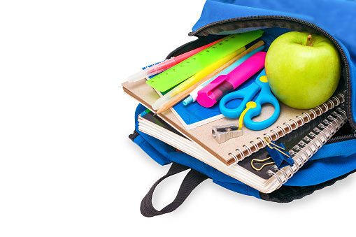 The students blue open schoolbag is filled with notebooks, pens, markers, stationery and a green apple lies on its side, isolated on a white background. Concept back to school, education, knowledge.