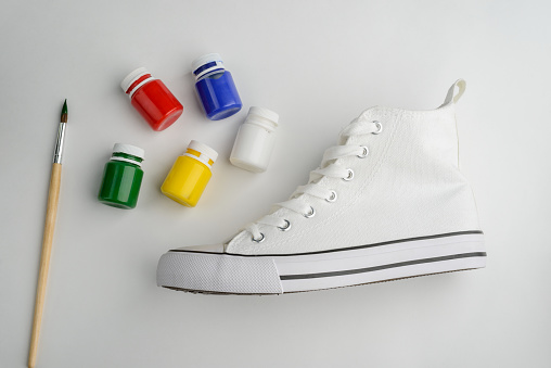 Brush, paint and blank canvas sneaker on white background. Creative project, use imagination to refashion boring shoes.
