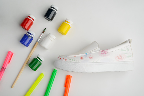 Leather slip-on shoes with painted flowers on white background. Beautiful art to makeover boring casual footwear.