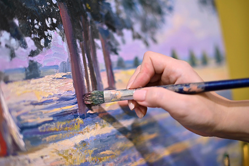 The artist s hand with a brush glides over the canvas of the painting. Close-up, brush strokes