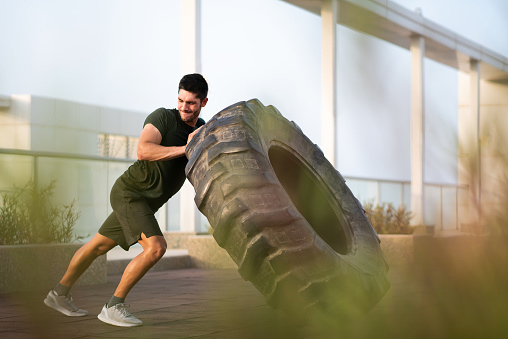 Muscular body builder flipping a tractor tire. Man exercising outdoors for a healthy fitness lifestyle