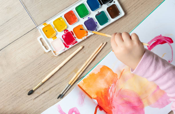 istock Child hand with brushes drawing on white paper. Child drawing top view 1254363866