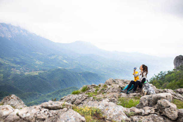 Young mom drinking water while enjoying the view from a mountain with her young son stock photo