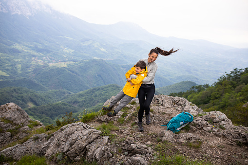 A young woman is smiling while swinging a cute boy side to side on a mountain with a beautiful view