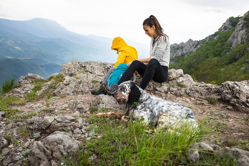 A mom and her son are sitting on rocks on a mountain ridge opening their backpacks