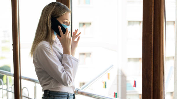 istock Distraught woman with face mask talking by the window 1254366804