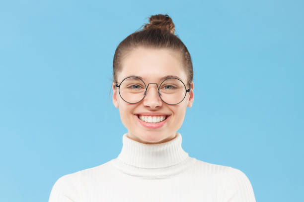 Close up portrait of smiling teen girl wearing white sweater and round glasses, isolated on blue background Close up portrait of smiling teen girl wearing white sweater and round glasses, isolated on blue background turtleneck photos stock pictures, royalty-free photos & images