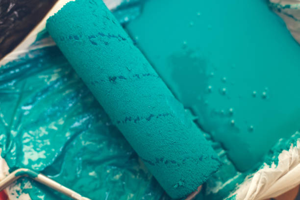 Paint roller in a tray with blue paint.