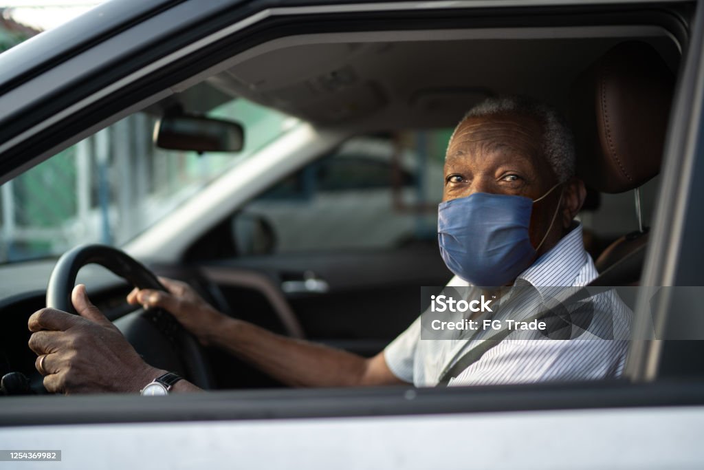Portrait of senior african man driving a car with face mask Driving Stock Photo