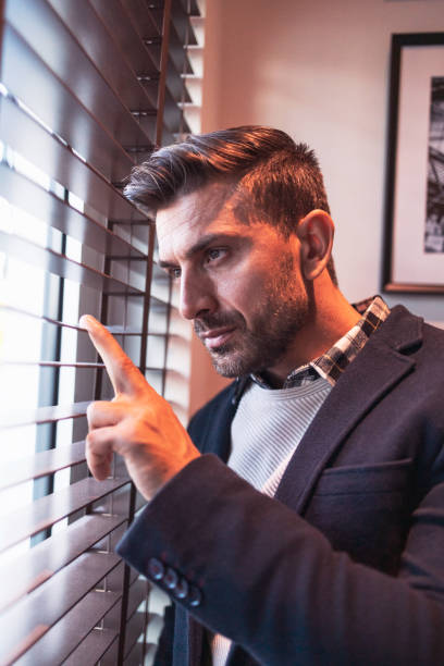 istock Portrait of a caucasian man looking through window blinds 1254372739