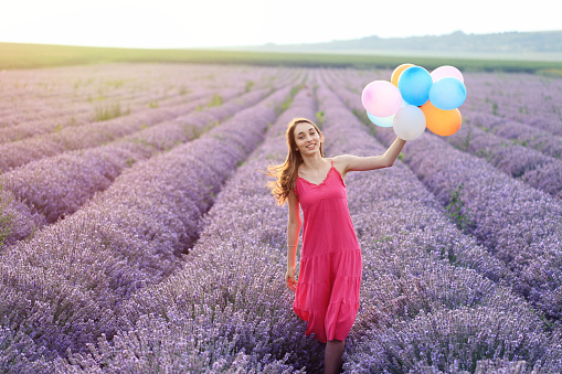 Happy young girl in lavender field holding colourful balloons