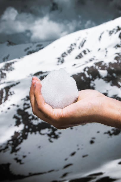 istock A hand holding snowball. Snow covered mountain background. 1254375395