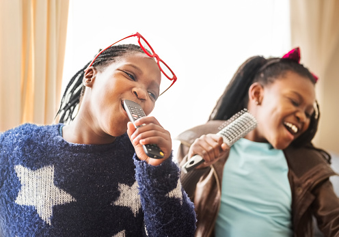 Shot of two girls singing together and having fun at home