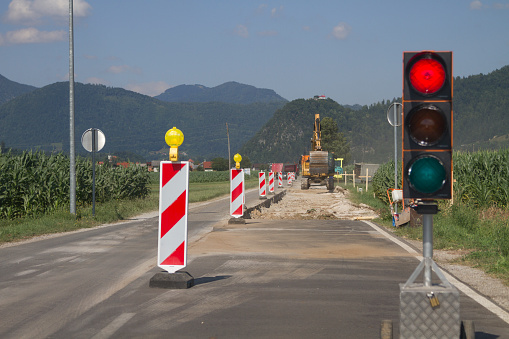 Mobile traffic light with a red luminous signal on the repair section of the road on the backdrop of a landscape with a blue and sunny sky.