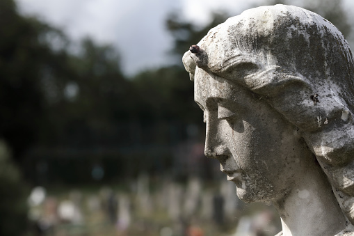 Bright sunlight with dark clouds in the background of this photo of a cemetery angel statue.
