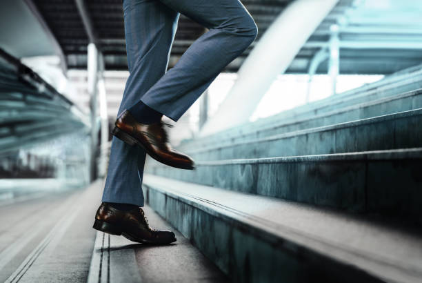 istock Motivation and challenging Concept. Steps Forward into a Success. Low Section of Businessman Walking Up on Staircase 1254395616