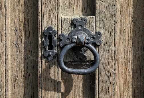 Wooden chapel door with cast iron round handle and door knocker, and cast metal escutcheon with upside-down keyhole. Close up.