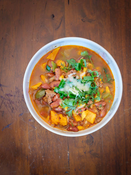 Chili with sweet potato, scallion and cheese served in a round bowl on rustic table
