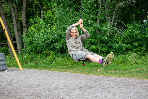 Mature woman with glasses riding a zip-line at an outdoor playground at a public park and recreation area in Jarfalla Sweden.