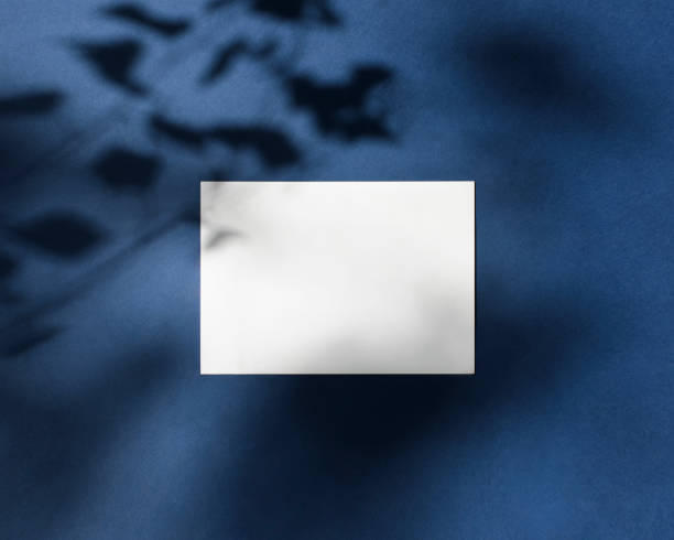 istock Empty white paper a5 mock up with leaves shadows on blue background. Classic Blue Pantone color. Holiday marketing, greeting card, invitation. Flat lay, top view. Branding identity. Add your text. 1254405436