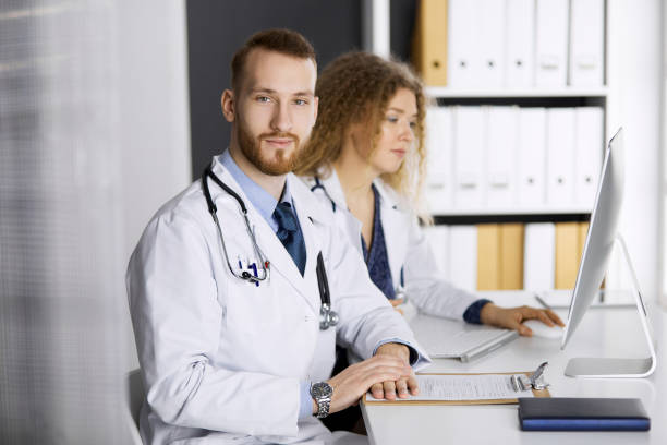 istock Red-bearded doctor with female colleague discussing current disease therapy while sitting at working place in clinic. Team work in medicine 1254406018