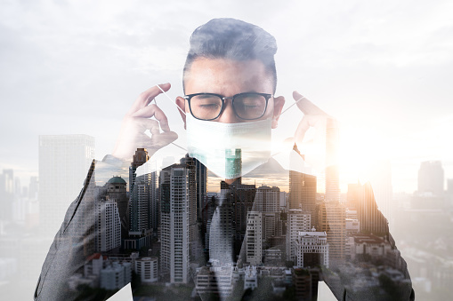 the double exposure image of the businessman wearing the medical mask and overlay with cityscape image. the concept of covit-19, work at home, quarantine, healthcare and business.