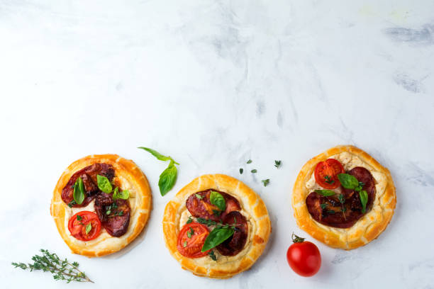 istock Mini tarts with dried meat, tomatoes, ricotta, thyme, basil and olives on a light background. Selective focus.Top view 1254407046