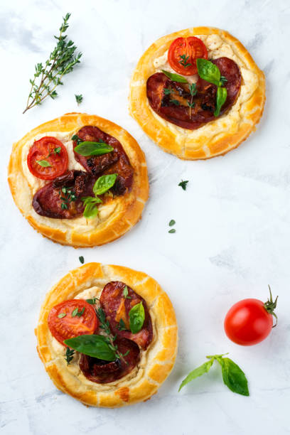 istock Mini tarts with dried meat, tomatoes, ricotta, thyme, basil and olives on a light background. Selective focus.Top view 1254407063
