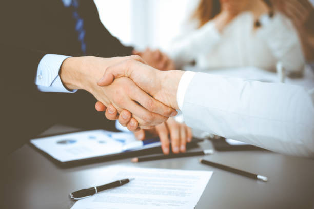 istock Business people shaking hands at meeting while theirs colleagues clapping and applauding. Group of unknown businessmen and women in modern white office. Success teamwork, partnership and handshake concept 1254407169